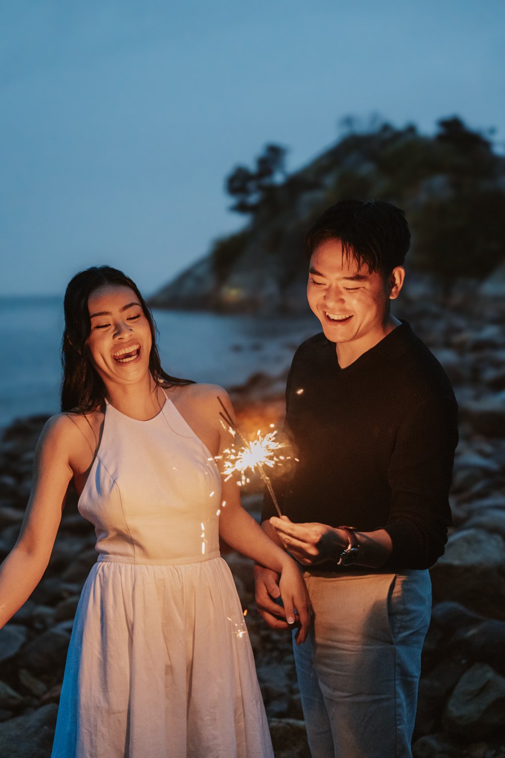 Aneeta and Christian laughing with sparklers on the shore at blue hour