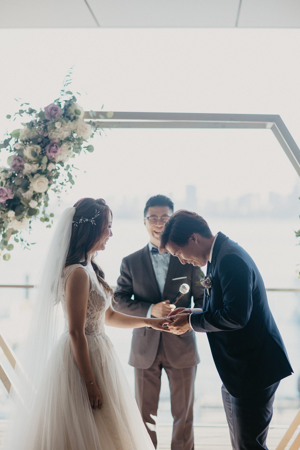 Rings exchanged under a hexagonal floral arch with the water visible behind