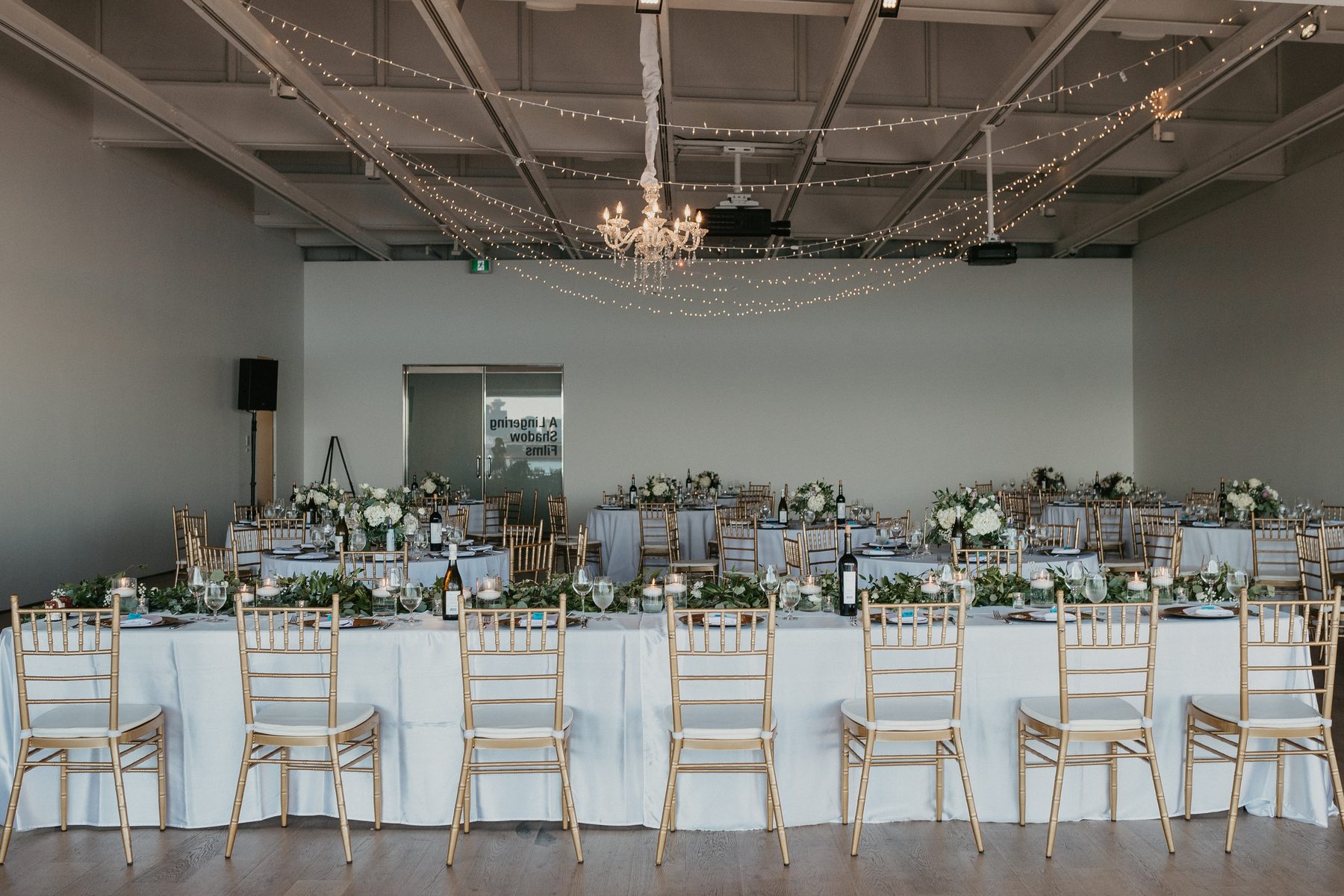 Long reception table dressed with greenery under a canopy of fairy lights