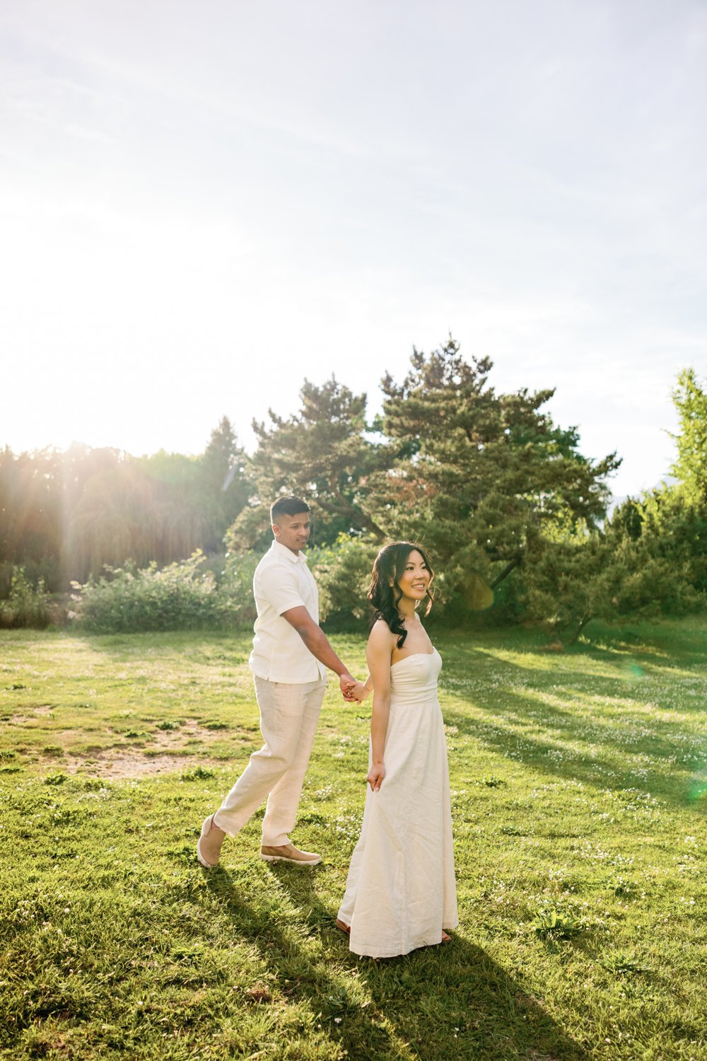 Eunice and Ashan in white, backlit on a golden lawn near UBC