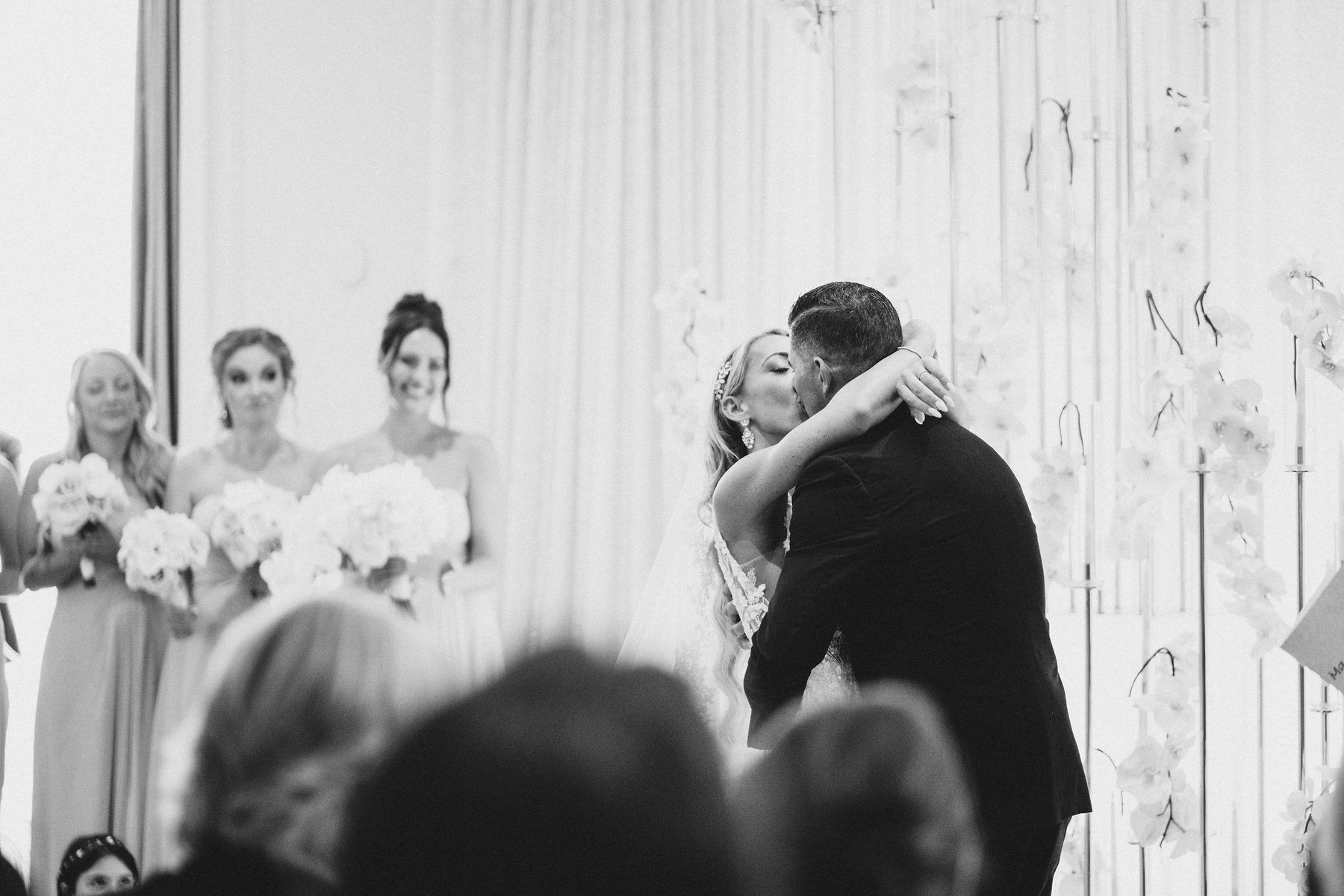 Black and white photograph of the couple kissing surrounded by their guests