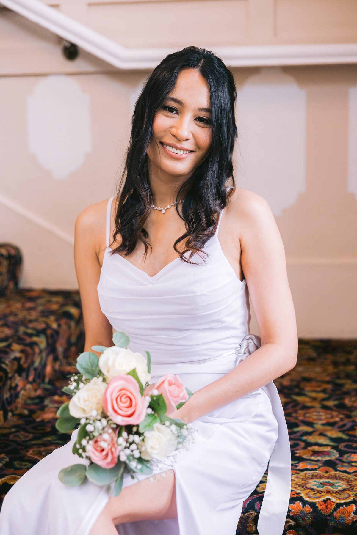 Bride seated on a wide carpeted staircase with leaded glass windows rising behind her
