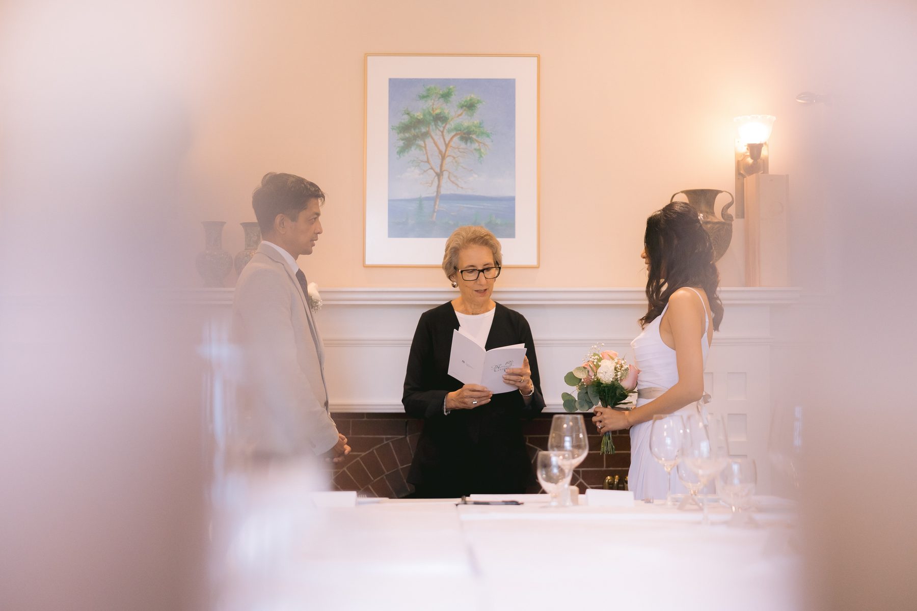 Couple standing before their officiant in a small restaurant dining room as guests look on
