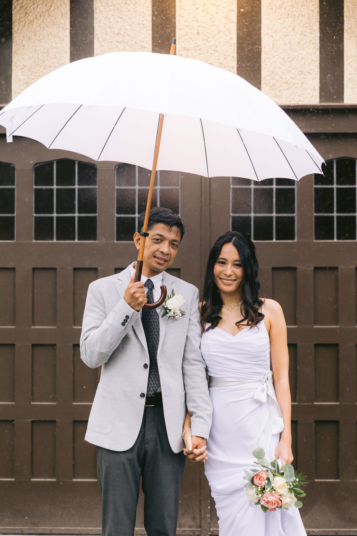 Couple sheltering under a white umbrella in front of the dark timber doors of the heritage house