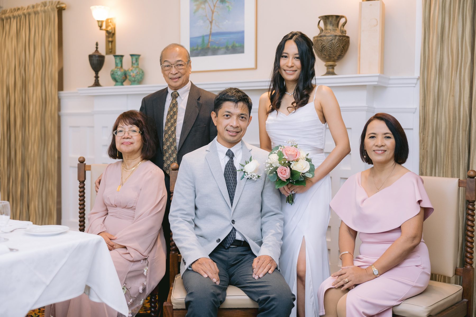 Family members gathered shoulder to shoulder in front of a white fireplace with the couple in the centre