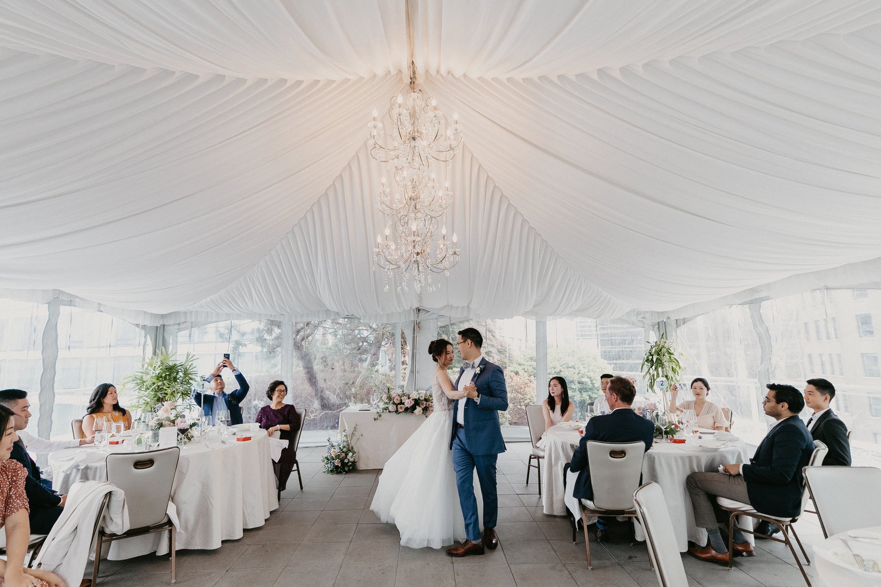 First dance under the chandeliers, guests watching from the tables