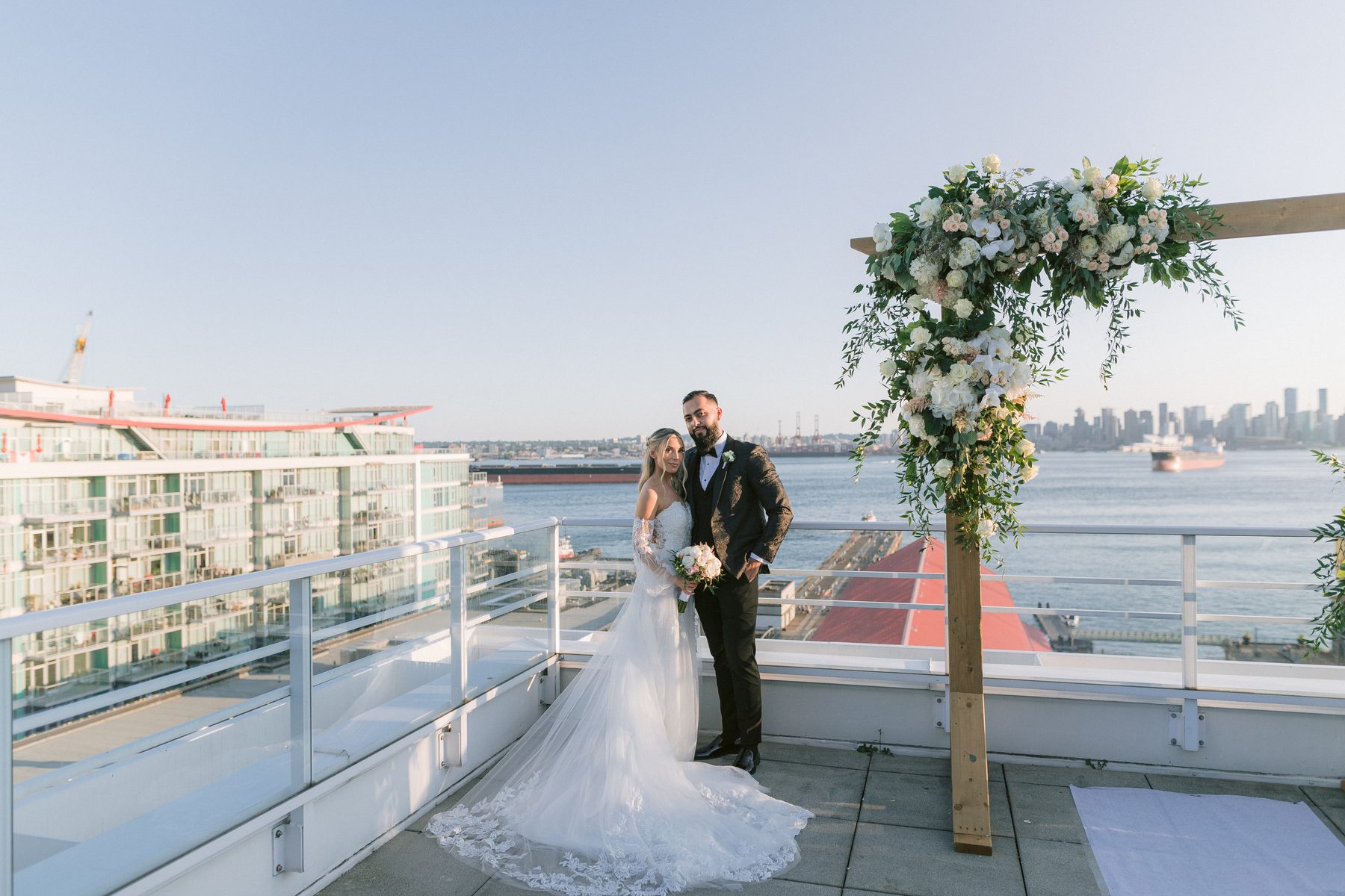 Bride and groom on an open rooftop deck with Burrard Inlet and the downtown Vancouver skyline behind them