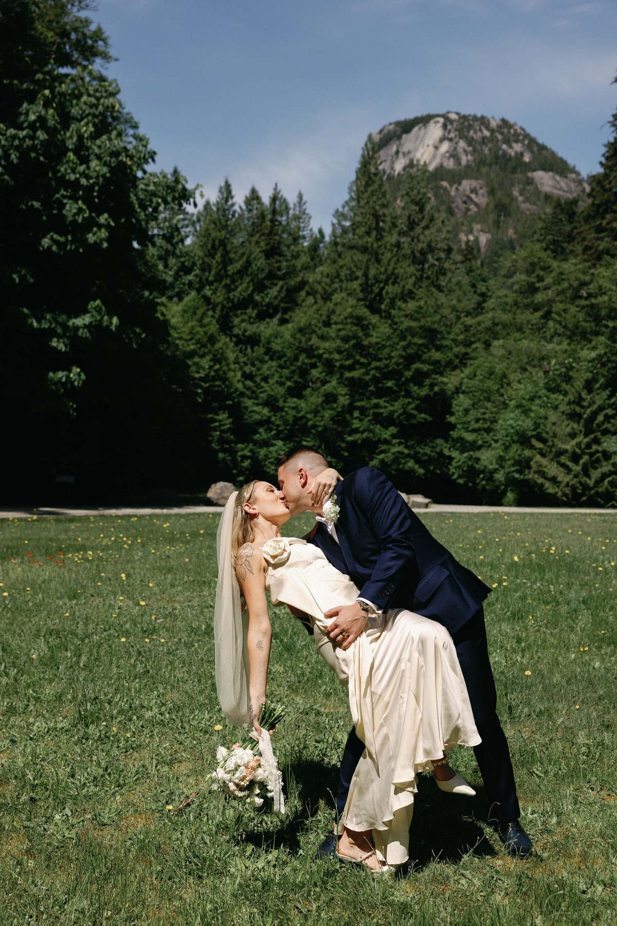 Groom dipping his bride for a kiss on the grass beneath the mountains