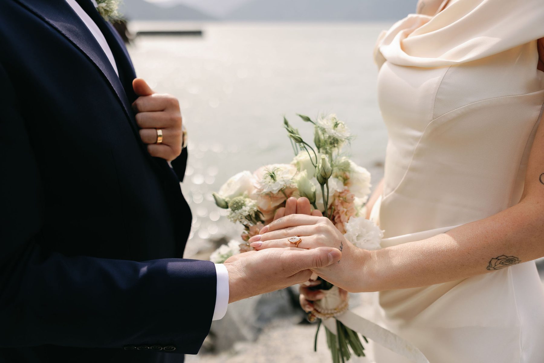 Groom's hand holding the bride's, wedding rings and white bouquet in frame
