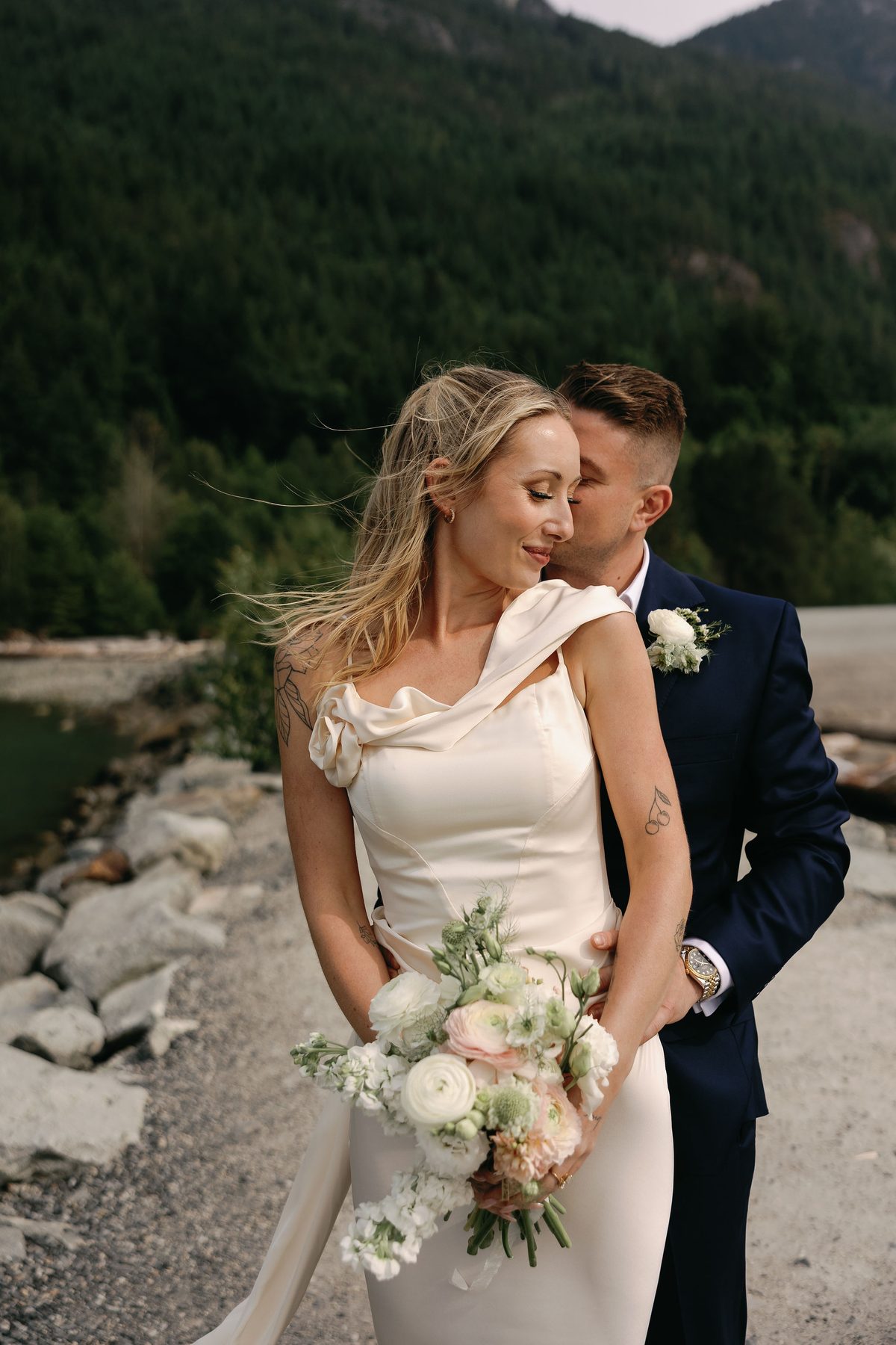 Couple standing together on a rocky shoreline in their wedding clothes