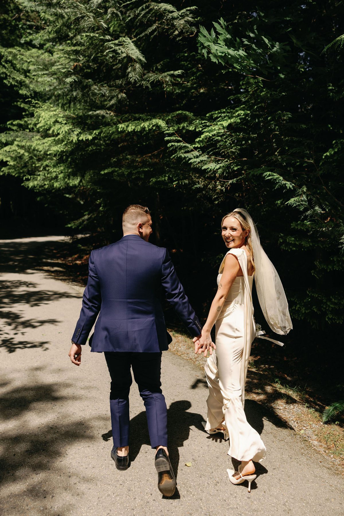 Bride and groom walking away down a tree-lined path, seen from behind