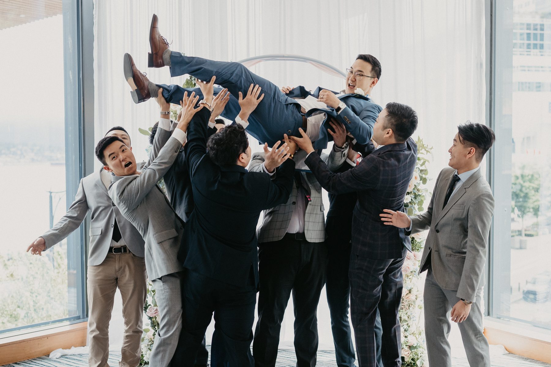 Groomsmen hoisting the groom into the air on the terrace while everyone laughs