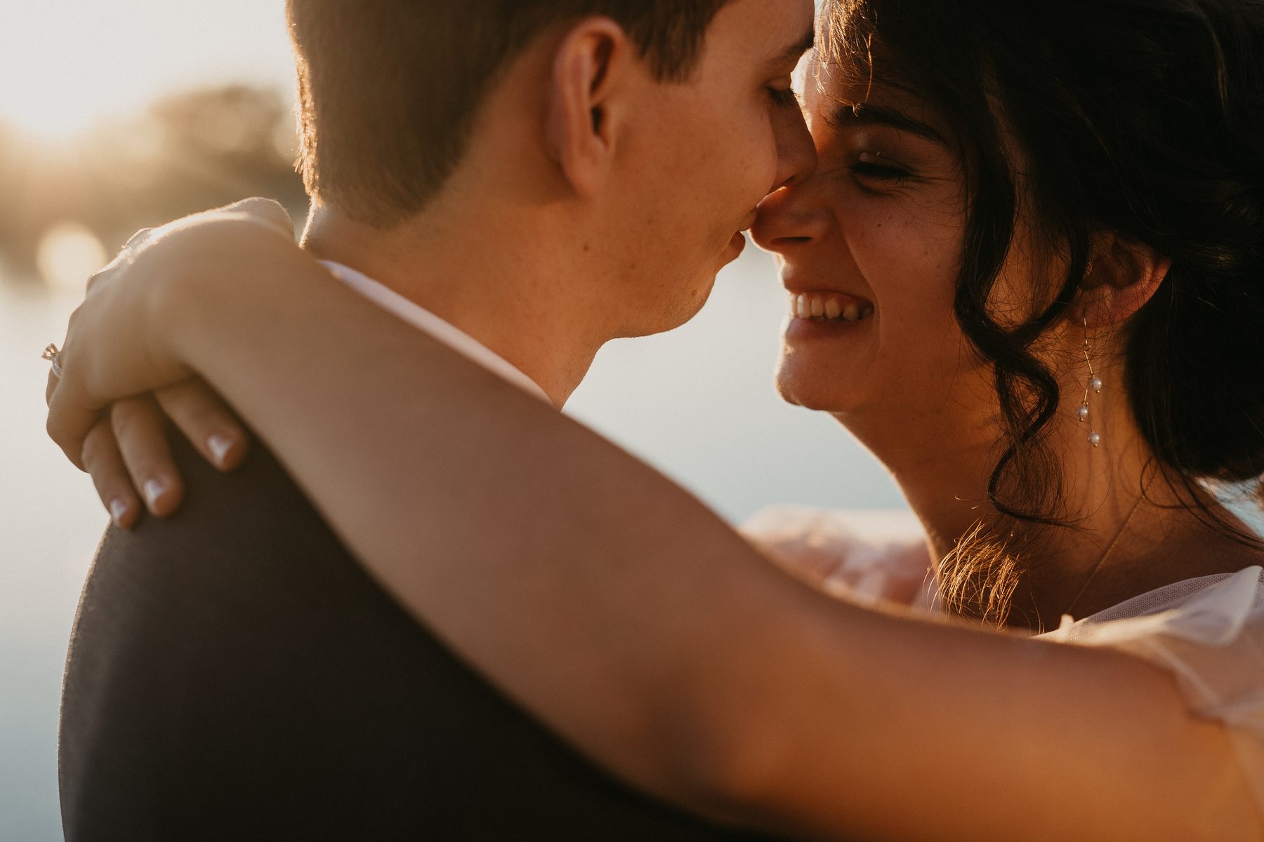 Couple holding each other at the end of a dock as the sun sets low over flat river water