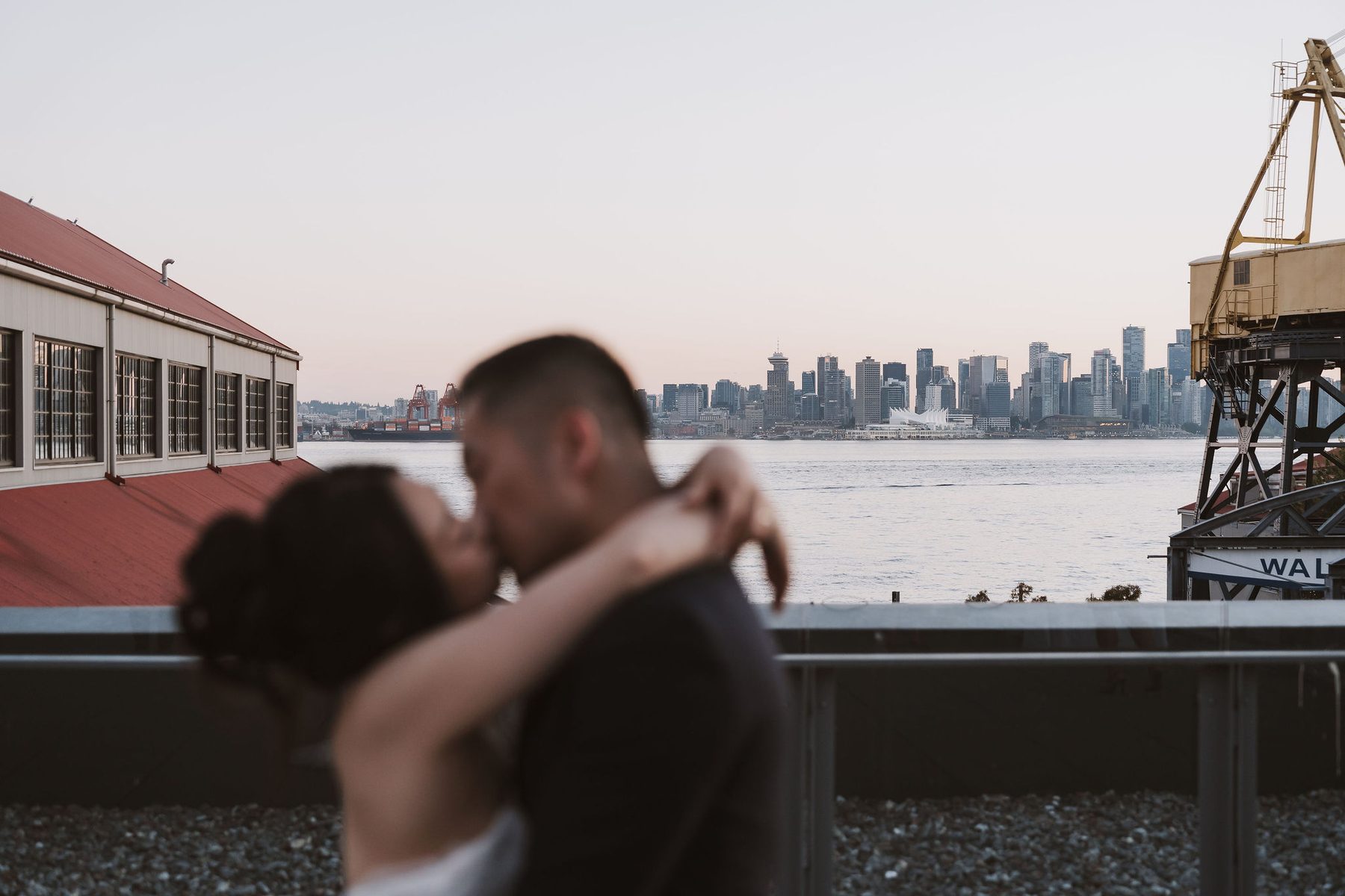Groom dipping his bride at dusk, city lights behind them