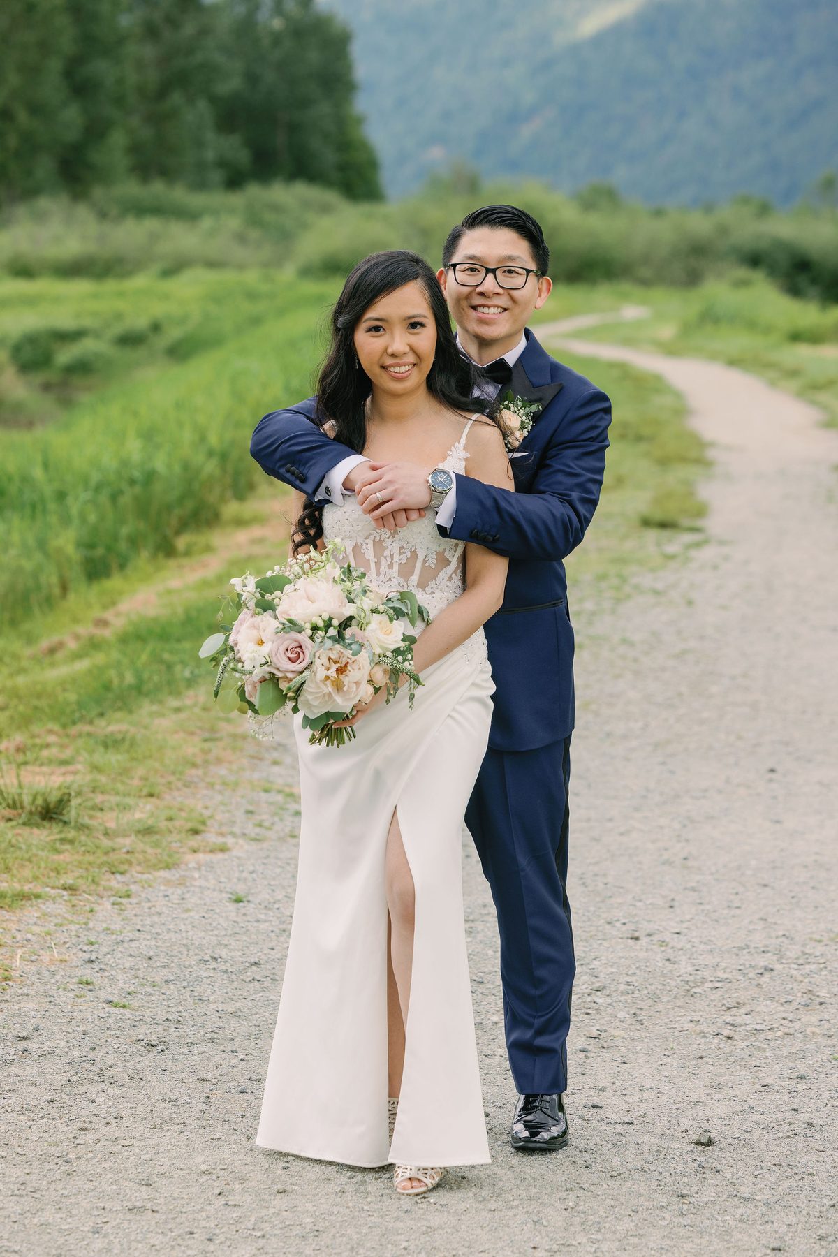 Couple walking a gravel path in spring, green marsh and mountains behind them