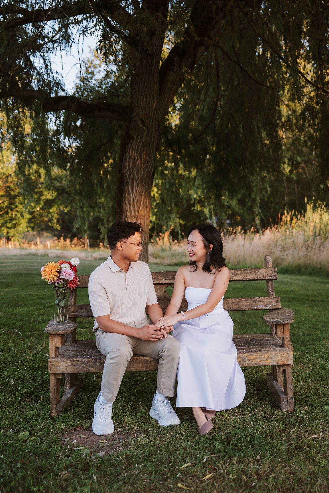 Couple sitting on a bench under a willow tree in the late summer sun