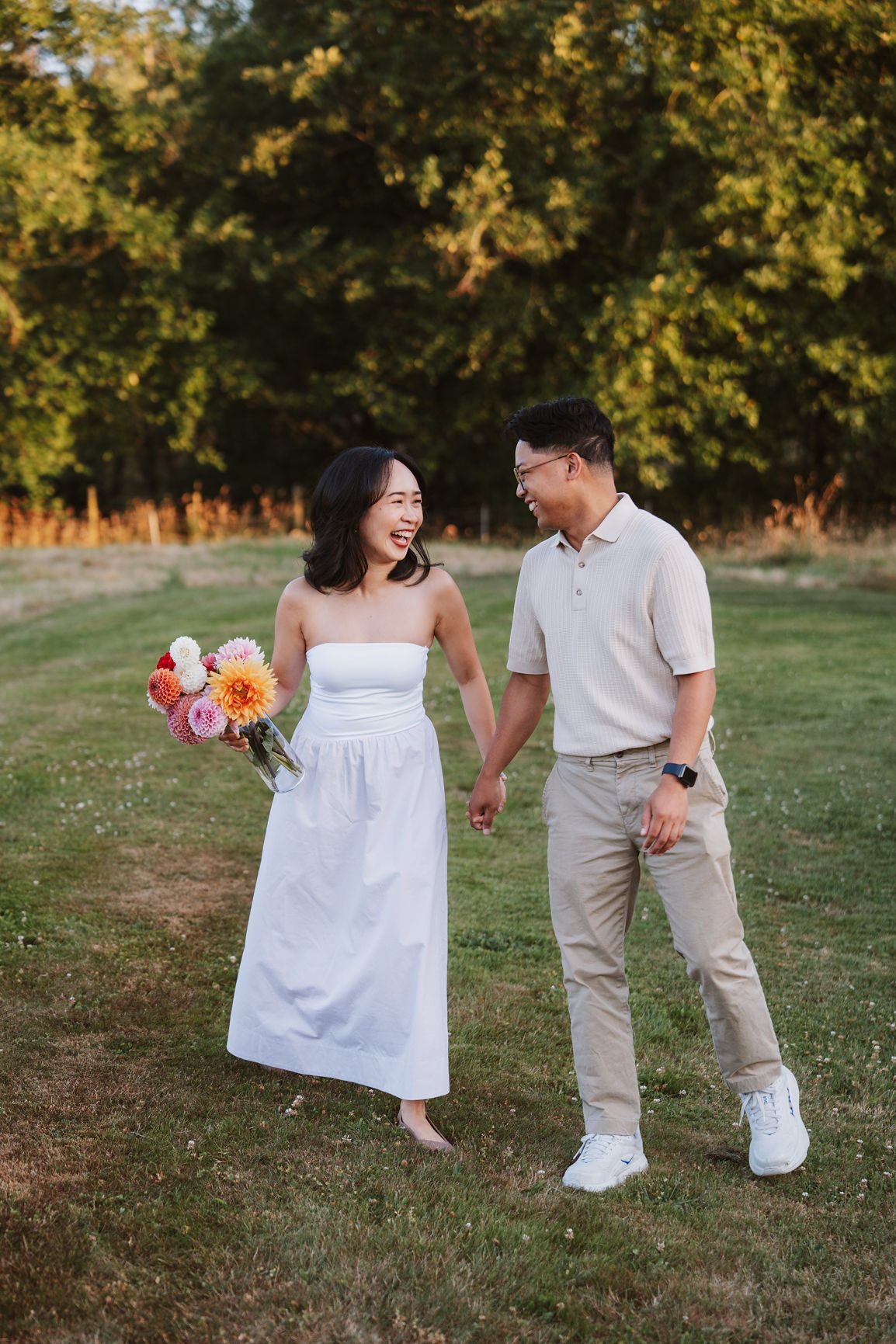 Couple walking through a farm field at sunset holding a bunch of dahlias