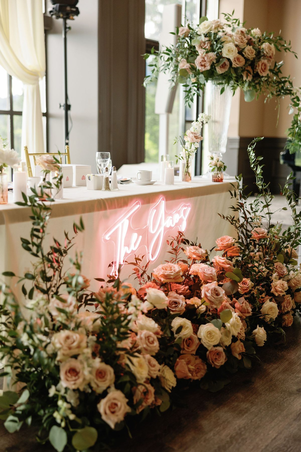 Sweetheart table backed by a neon sign and a wall of peach and coral florals