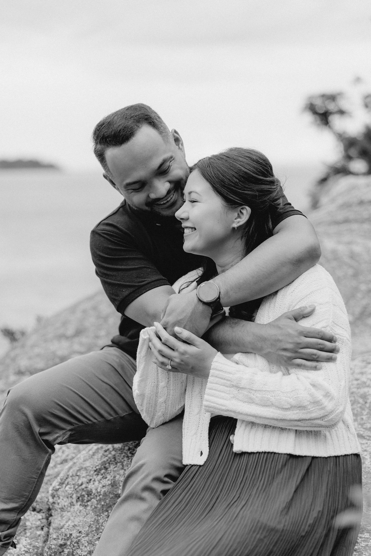 Black and white photograph of a couple laughing, her arms around his shoulders