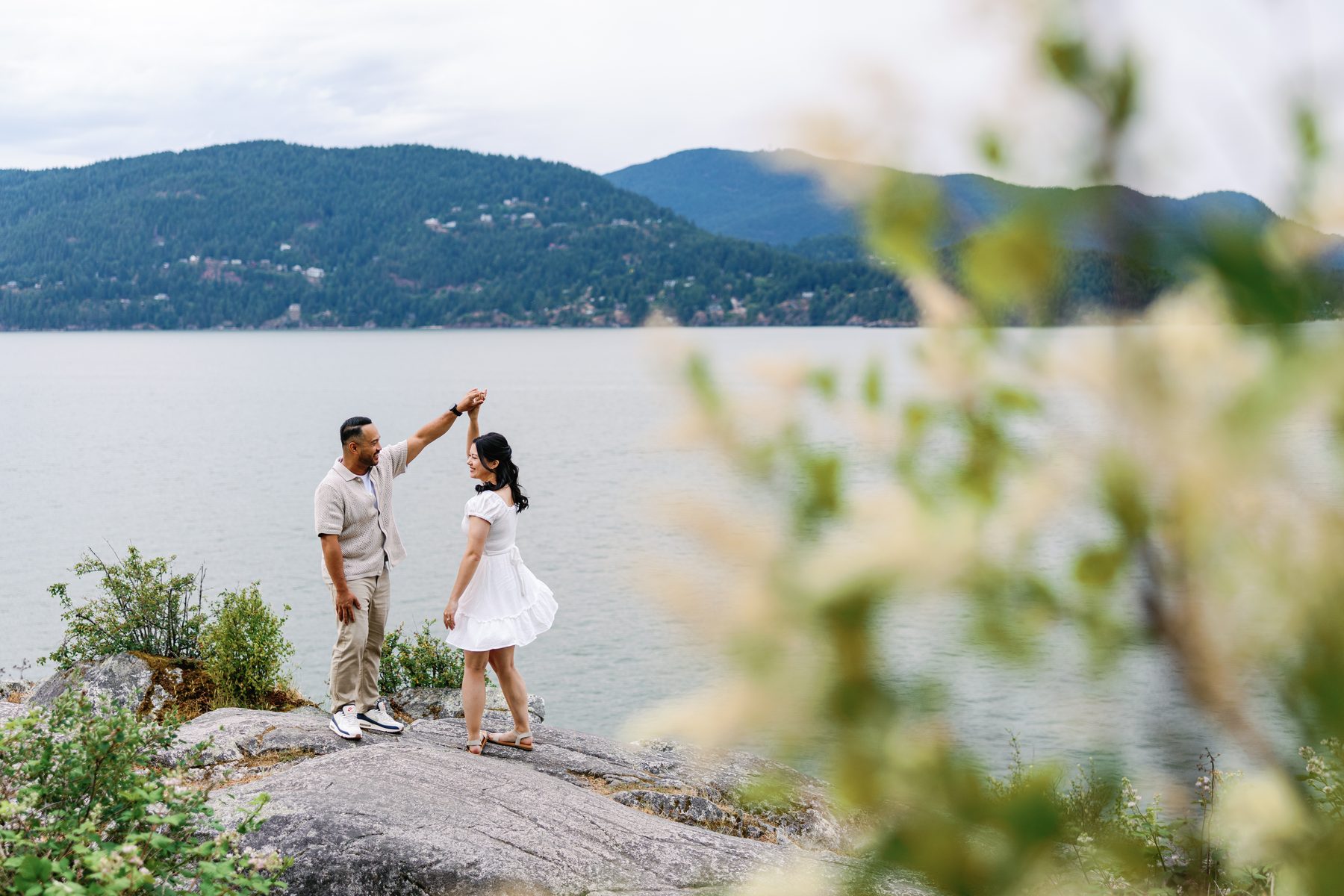 Couple dancing on the rocks, seen through the leaves of a foreground branch